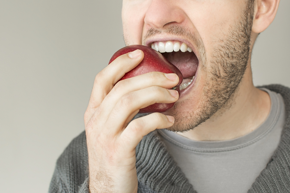 Man eating a red apple, showcasing healthy eating habits to support oral health and weight management.