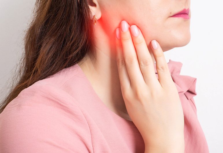 Woman experiencing dental pain, holding her jaw, emphasizing the urgency of dental emergencies related to knocked-out teeth.