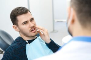 Patient experiencing dental pain while consulting with a dentist in a clinical setting, emphasizing the importance of immediate dental care for a knocked-out tooth.