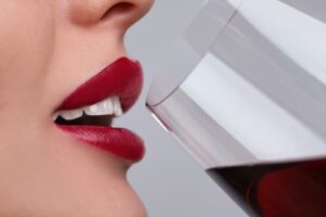 Close-up of a woman's lips with bold red lipstick, poised to sip from a glass of dark red mulled wine, highlighting potential dental health risks associated with holiday beverages.