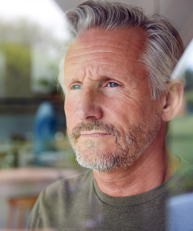 Thoughtful middle-aged man with gray hair and beard, reflecting on dental health and potential dental implant options.
