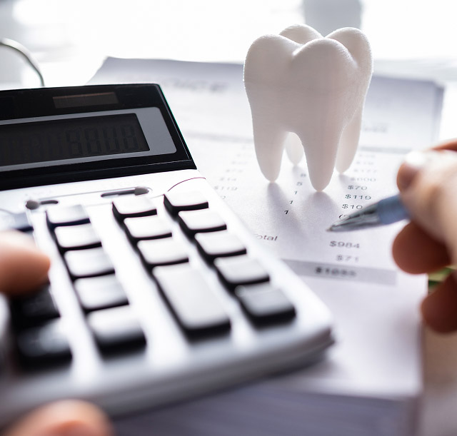 Calculator and dental model on financial documents, representing dental implant costs and budgeting for dental services.
